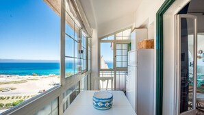 Un balcon avec vue sur la mer, une table blanche ornée d’un vase décoratif et une chaise blanche.