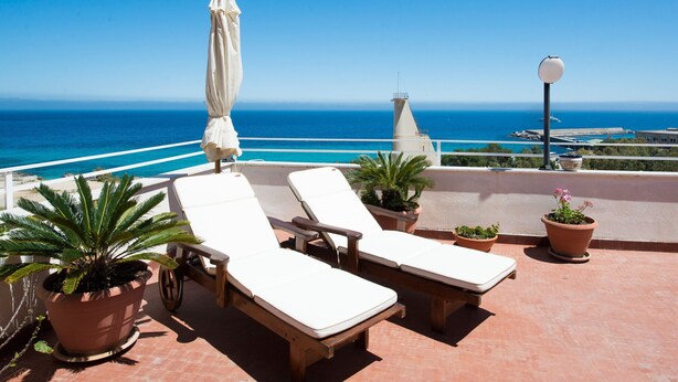 Une terrasse sur le toit avec deux chaises longues, un pot de fleurs et une vue sur l’océan.