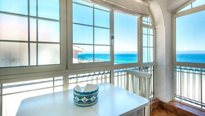 Une pièce dotée de grandes fenêtres donnant sur la mer, une table blanche ornée d’un vase décoratif et un plancher en bois.