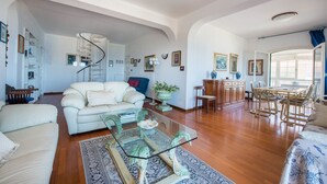 Un salon spacieux avec un canapé blanc, une table basse en verre et un coin repas comprenant une table et des chaises en bois.