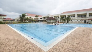 A large outdoor swimming pool with multiple lanes, surrounded by buildings with red roofs and palm trees. - Terengganu Equestrian Resort (Kuala Terengganu)
