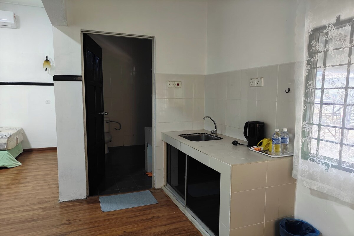 Una cocina pequeña con un lavamanos, una ventana con cortina decorativa y una puerta que da a otra habitación.