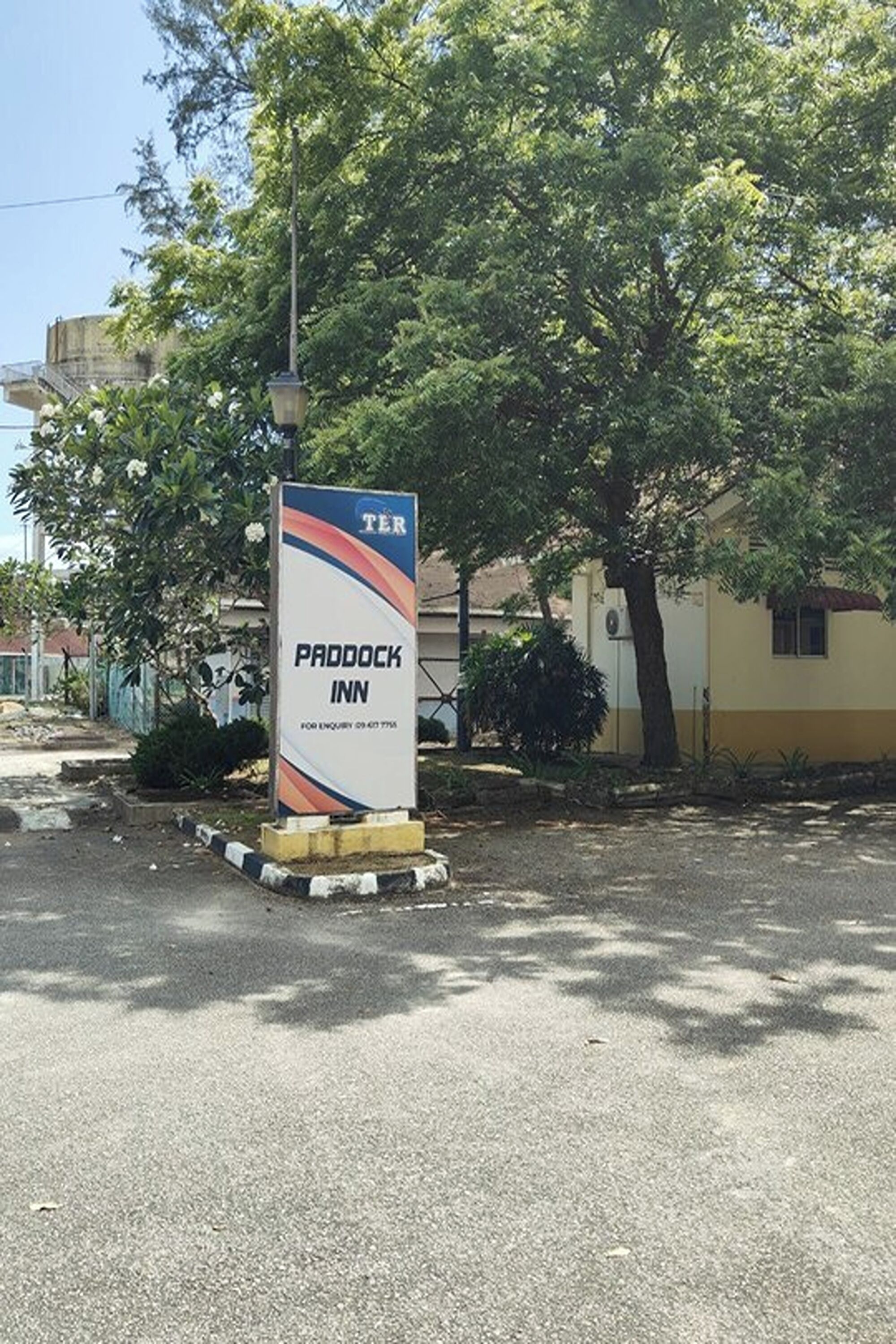 A sign for Paddock Inn with a tree and building in the background.