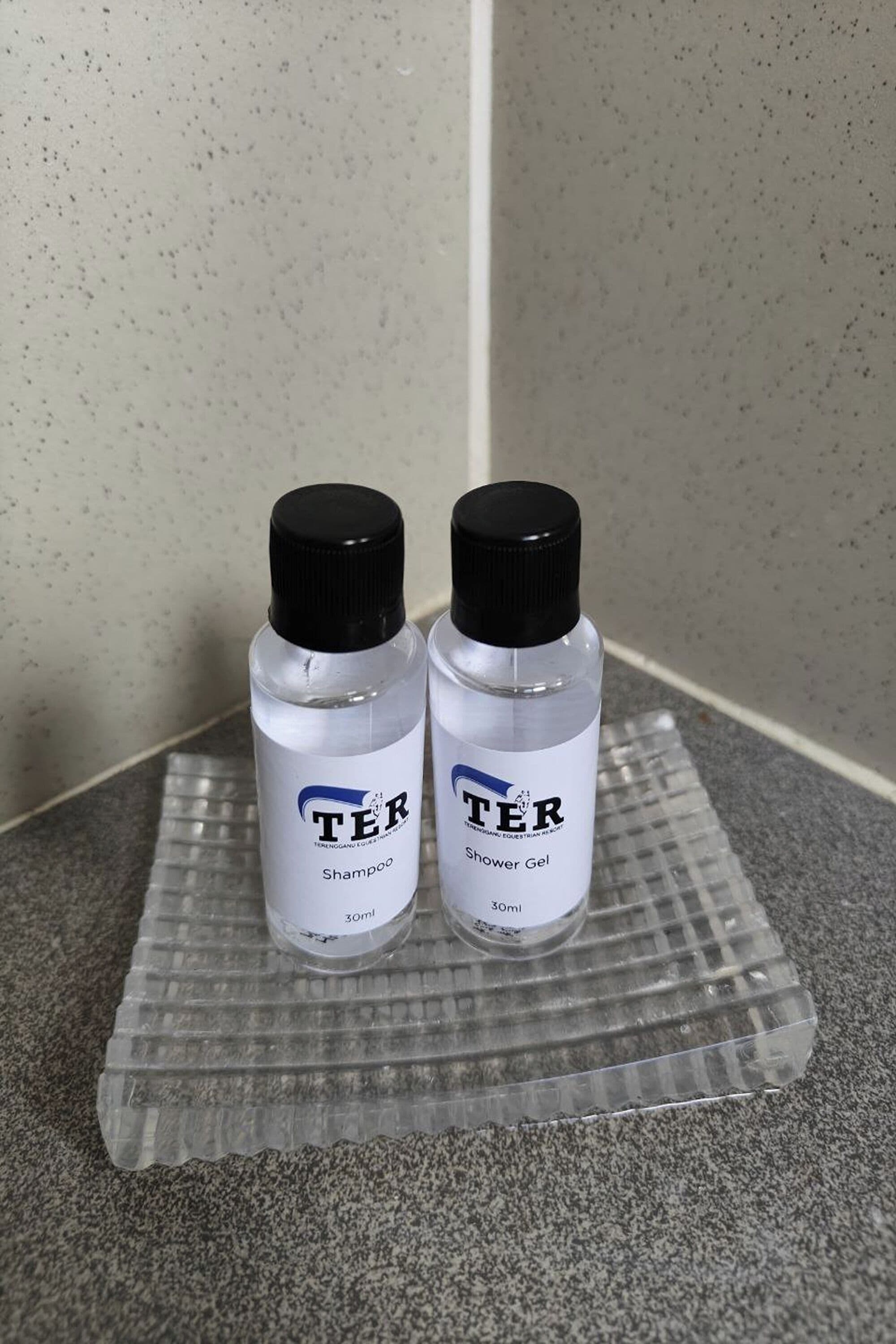 Deux flacons de shampoing et de gel douche de la marque TER, présentés sur un plateau transparent.