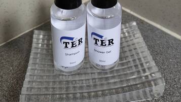 Deux flacons de shampoing et de gel douche de la marque TER, présentés sur un plateau transparent.