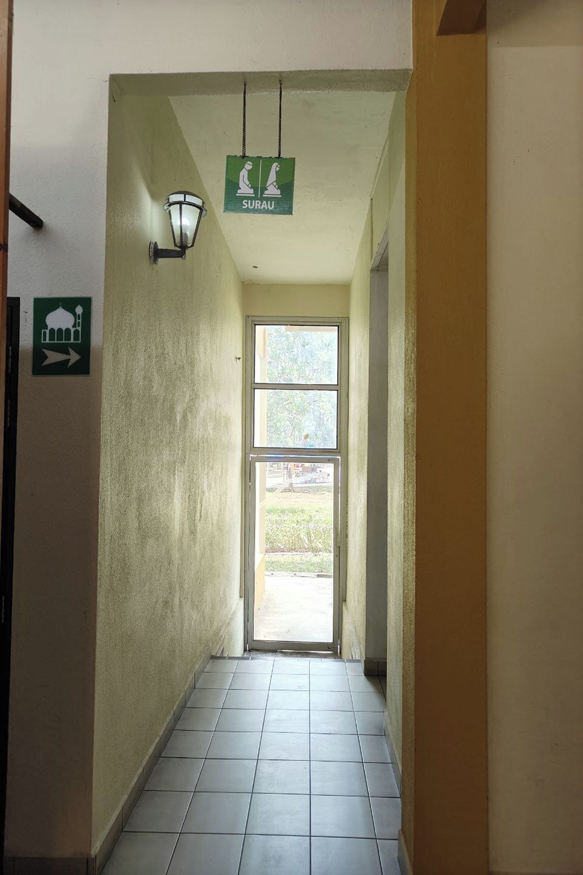A hallway with a tiled floor, a door at the end, and a sign above the door indicating a restroom.