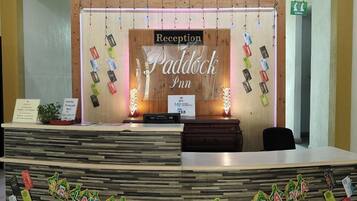 A reception desk with a wooden backdrop and a sign that reads "Reception Paddock Inn."
