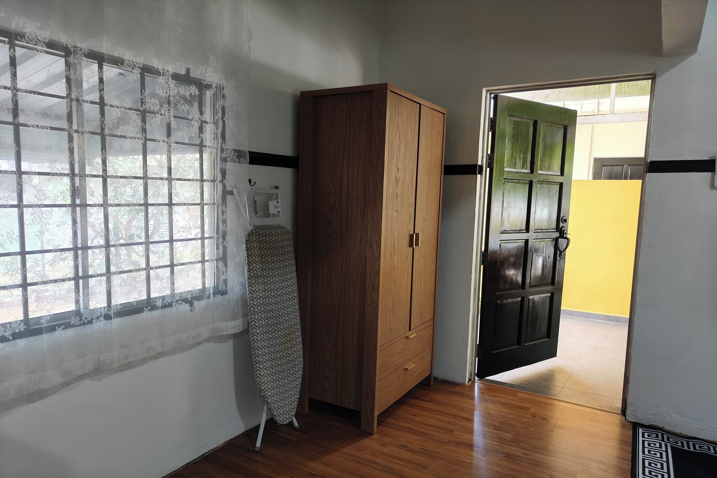Una habitación con un armario de madera, una ventana con cortina de encaje y una puerta que da a otra habitación.