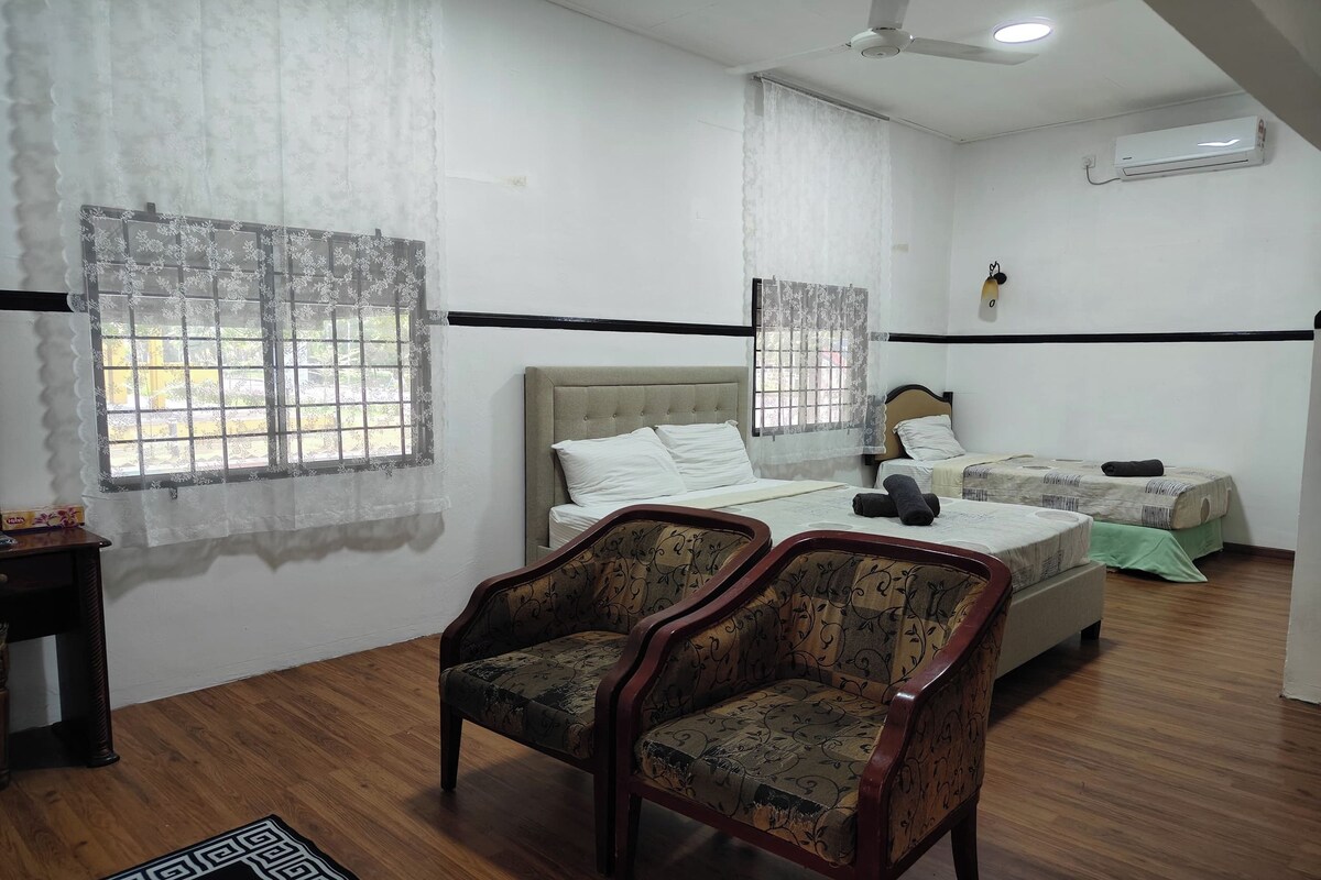 A hotel room with a bed, two chairs, a bedside table, and a window with curtains.