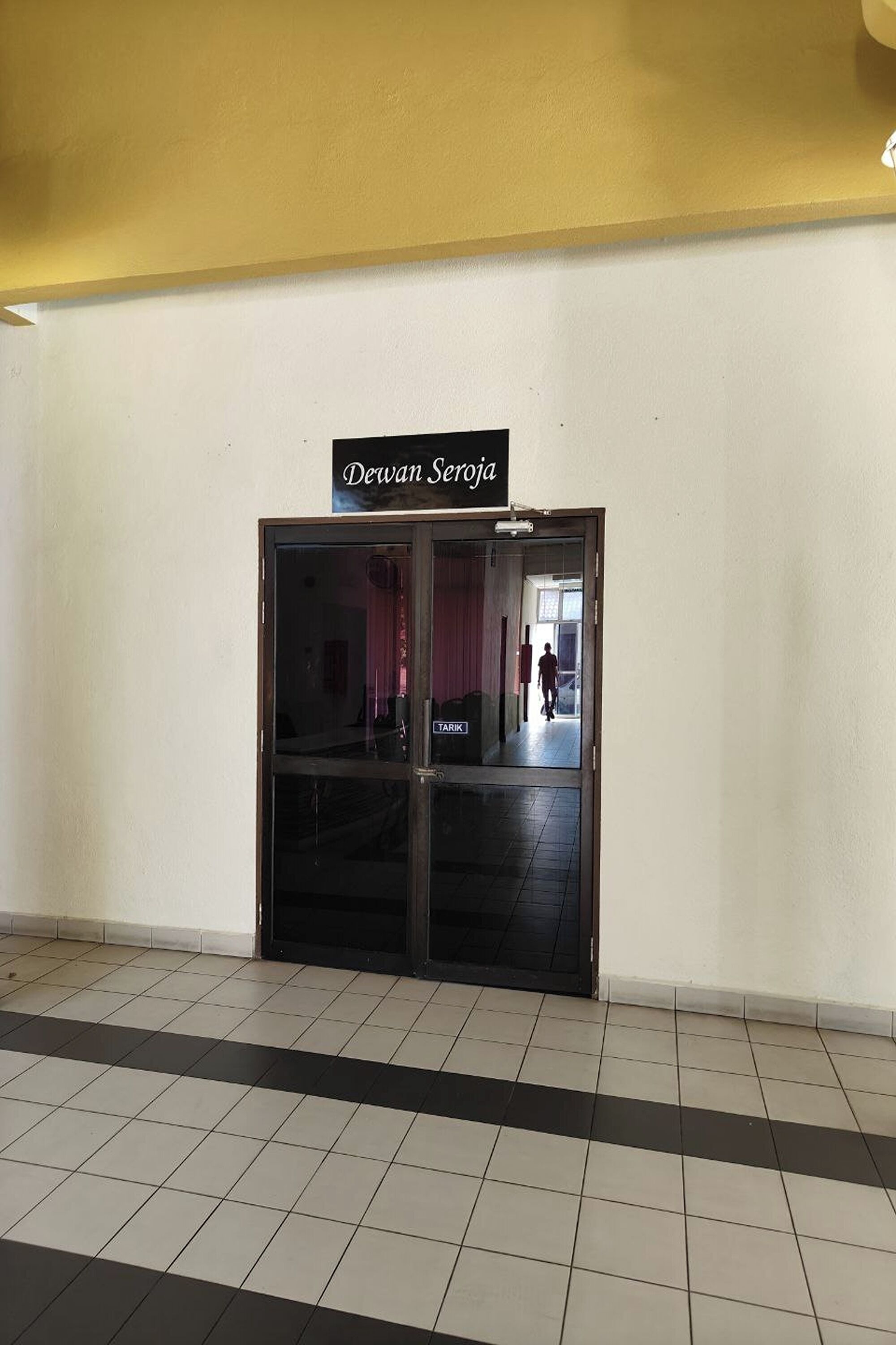A hotel entrance with a sign reading "Devan Seroja" and a visible "TRINK" sign inside.