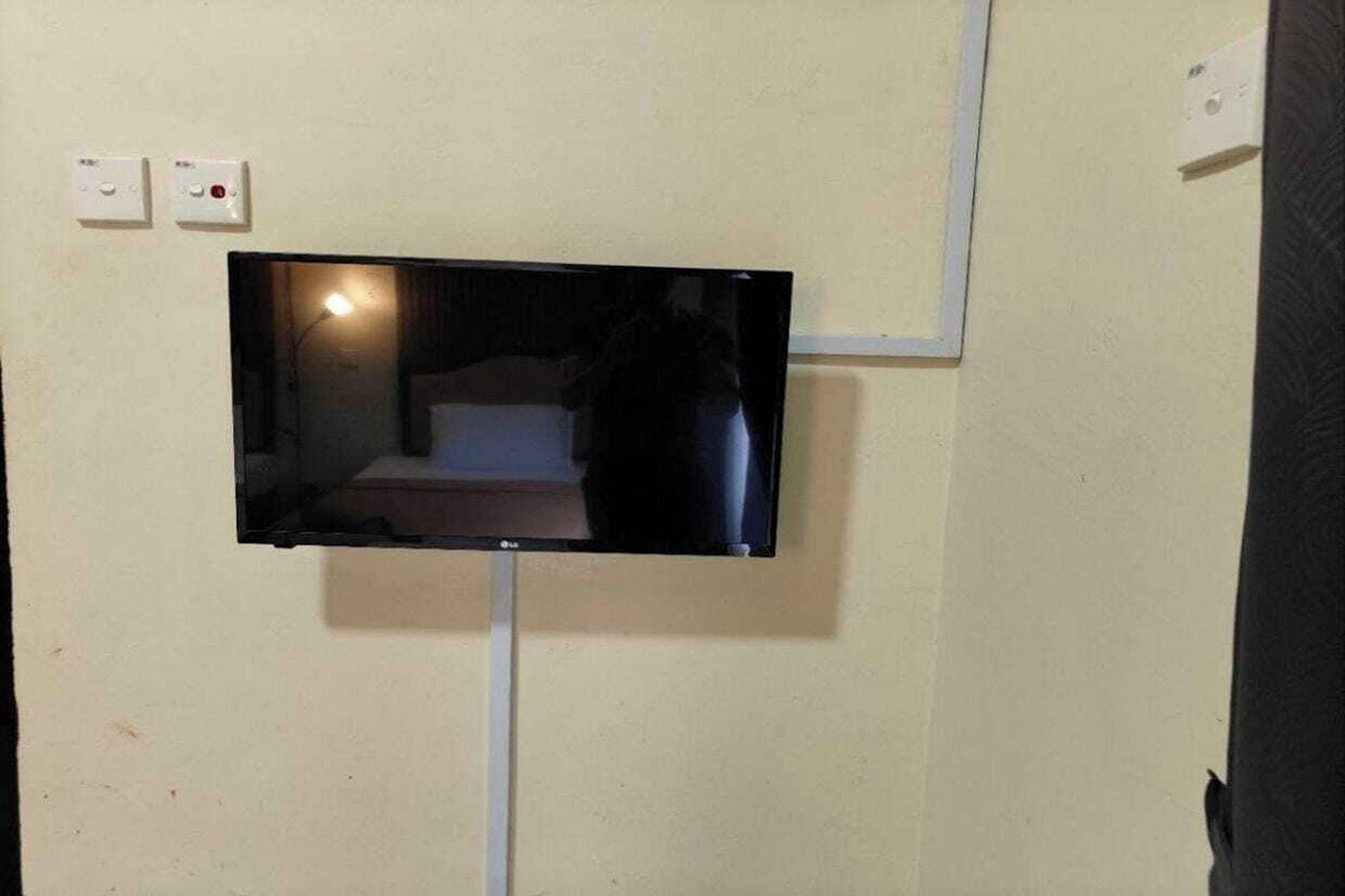 Un televisor de pantalla plana montado en la pared, con una cama visible en el reflejo.