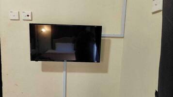 Un televisor de pantalla plana montado en la pared, con una cama visible en el reflejo.
