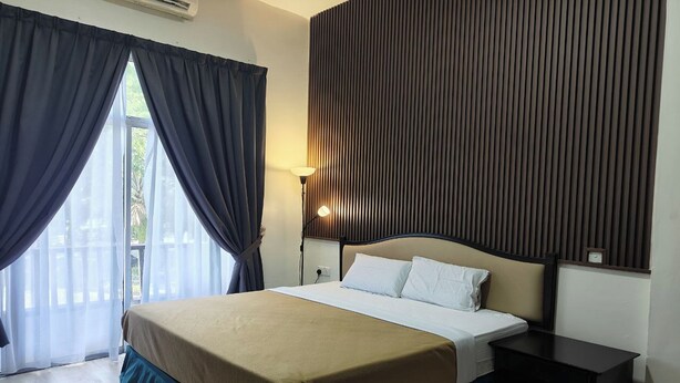 A hotel room with a bed, a nightstand, a lamp, and a view of the outdoors through a window with curtains. - Terengganu Equestrian Resort (Kuala Terengganu)