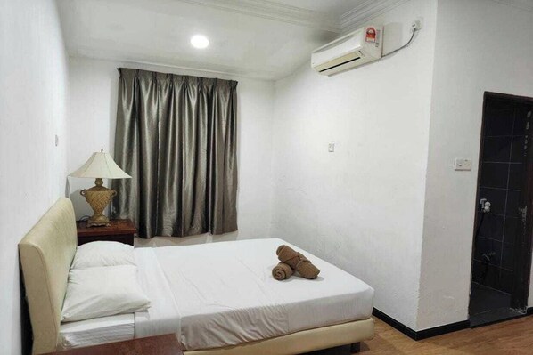 A hotel room with a bed, a nightstand with a lamp, a window with curtains, and an air conditioning unit.