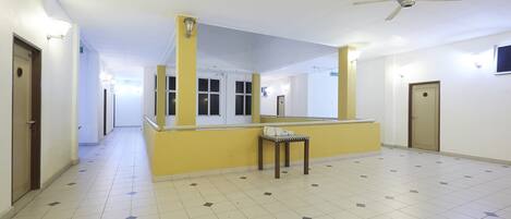 A hallway with a yellow accent wall, a ceiling fan, and a tiled floor.