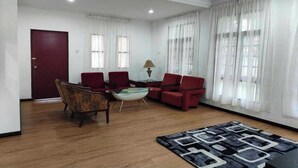 A spacious living room with a red door, two red armchairs, a glass coffee table, a patterned armchair, and a black and white rug. - Terengganu Equestrian Resort (Kuala Terengganu)