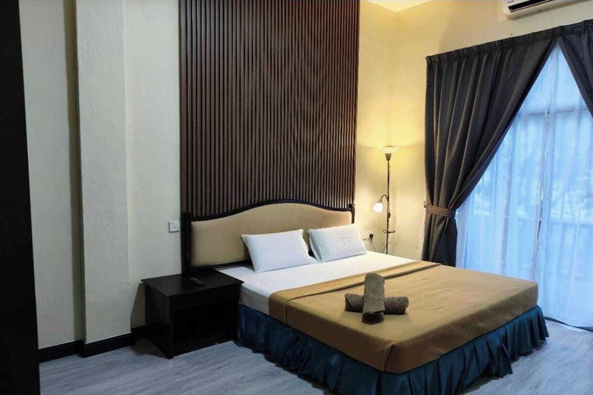 Habitación de hotel con una cama grande, una mesita de noche, una lámpara de pared y un ventanal con cortinas.
