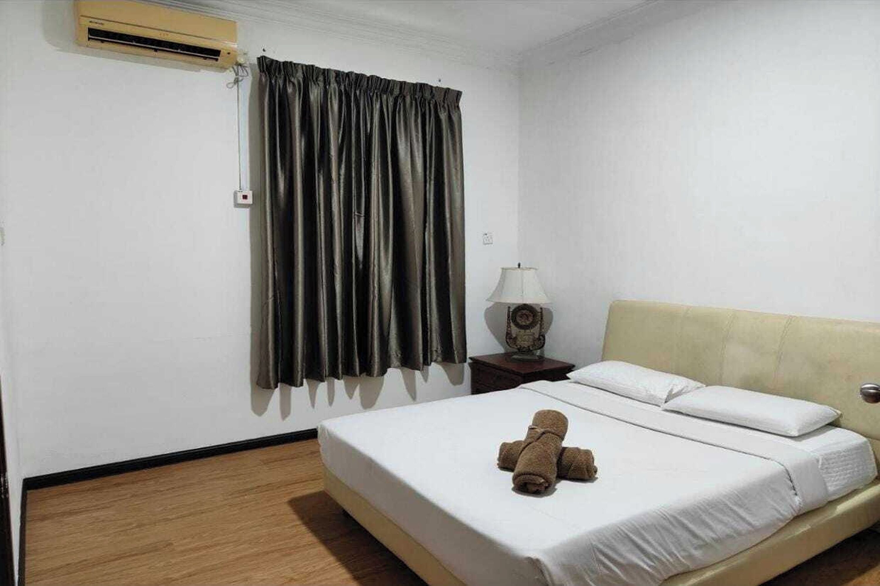 A hotel room with a bed, a nightstand with a lamp, a window with curtains, and an air conditioning unit.