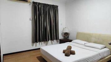 A hotel room with a bed, a nightstand with a lamp, a window with curtains, and an air conditioning unit.