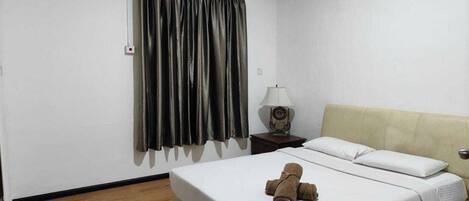 Habitación de hotel con cama, mesita de noche con lámpara, ventana con cortinas y equipo de aire acondicionado.