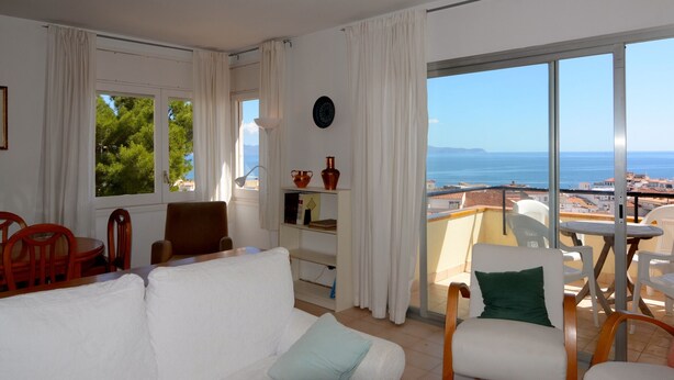Una habitación con sofá blanco, una mesa de comedor con sillas, vista al mar y un balcón con barandilla.