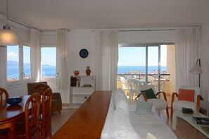 A modern living room with a wooden dining table, white sofa, and a view of the sea. - PUIG PADRO 6 1-4 (L'Escala)