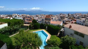 Un barrio residencial con piscina, casas de techo rojo y vista al mar y las montañas al fondo.