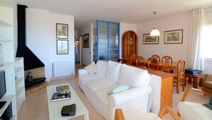 Una sala de estar con sofá, mesa de centro y chimenea. Hay un comedor con mesa y sillas.