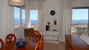 Un comedor con una mesa y sillas, una estantería y vista al mar.