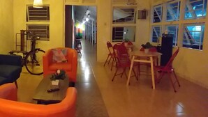 Uma sala de estar com sofá, uma poltrona laranja, uma mesa e uma área de refeições com cadeiras e mesa.