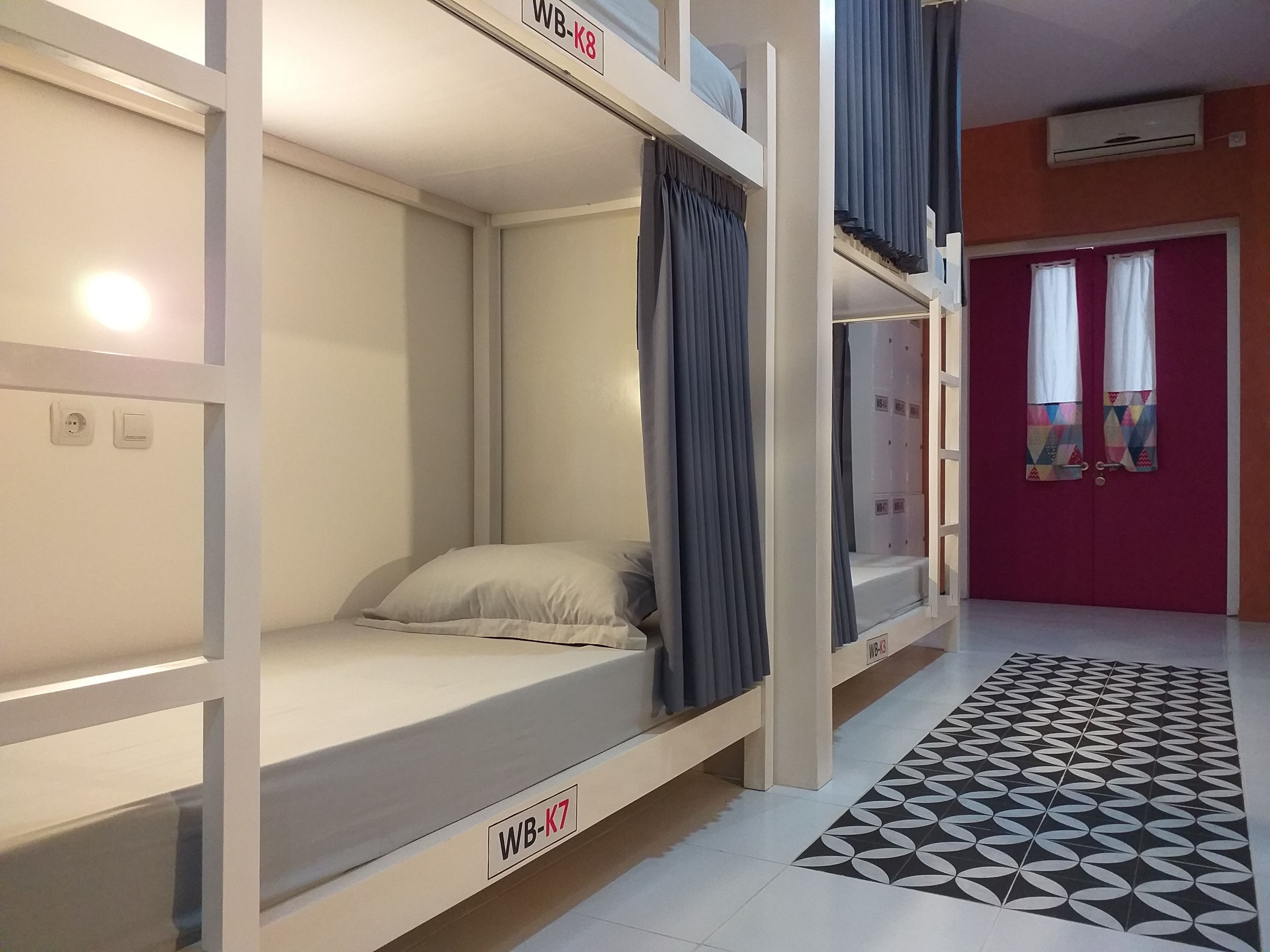 A dormitory room with bunk beds, a patterned floor, and a red door.