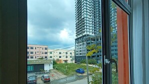 A view from a window overlooking a parking area with several cars, a building with a sign, and a tall residential building in the background.