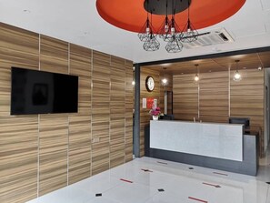 Un área de recepción moderna con una pared de madera, un televisor de pantalla plana, un mostrador de recepción y un reloj.