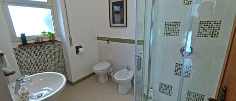 Une salle de bain avec une douche à parois de verre, un lavabo, deux toilettes et une fenêtre.