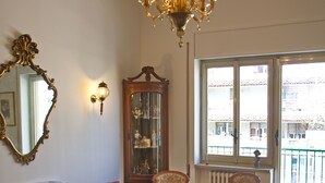 Una habitación con candelabro, un espejo grande, un armario de madera y vistas a edificios a través de una ventana.