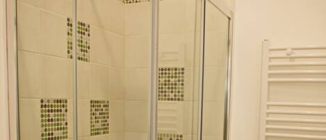 Una ducha con cerramiento de vidrio, piso de azulejos y toallero blanco.
