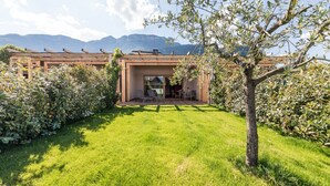 Een modern huis met een houten pergola, een gazon en een berg op de achtergrond.