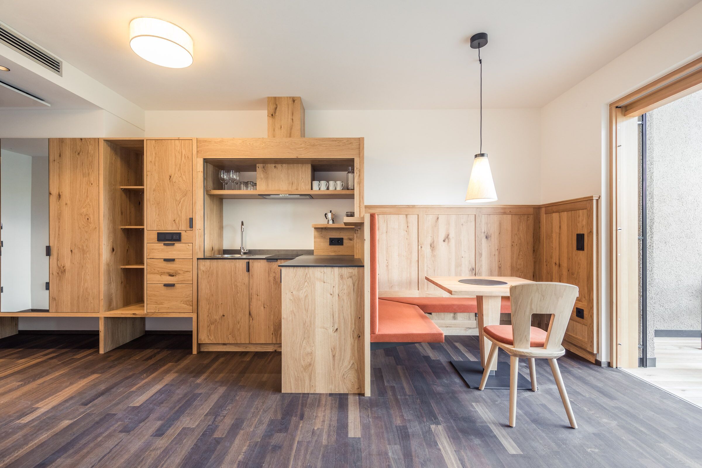 A modern kitchen with wooden cabinetry, a central island, and a dining area with a chair.