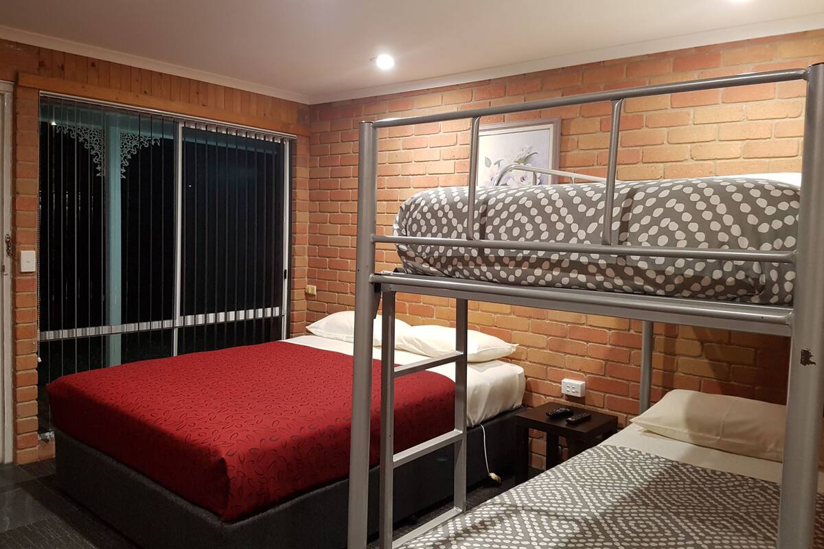 A bunk bed room with a red bedspread, a grey and white polka dot bedspread, and a brick wall.