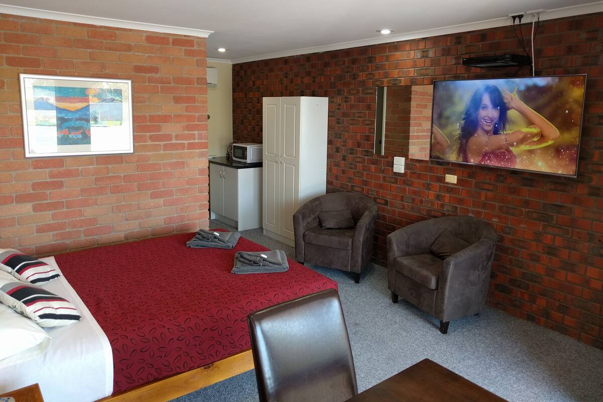 A room with a bed, two armchairs, a TV, a microwave, and a wardrobe.