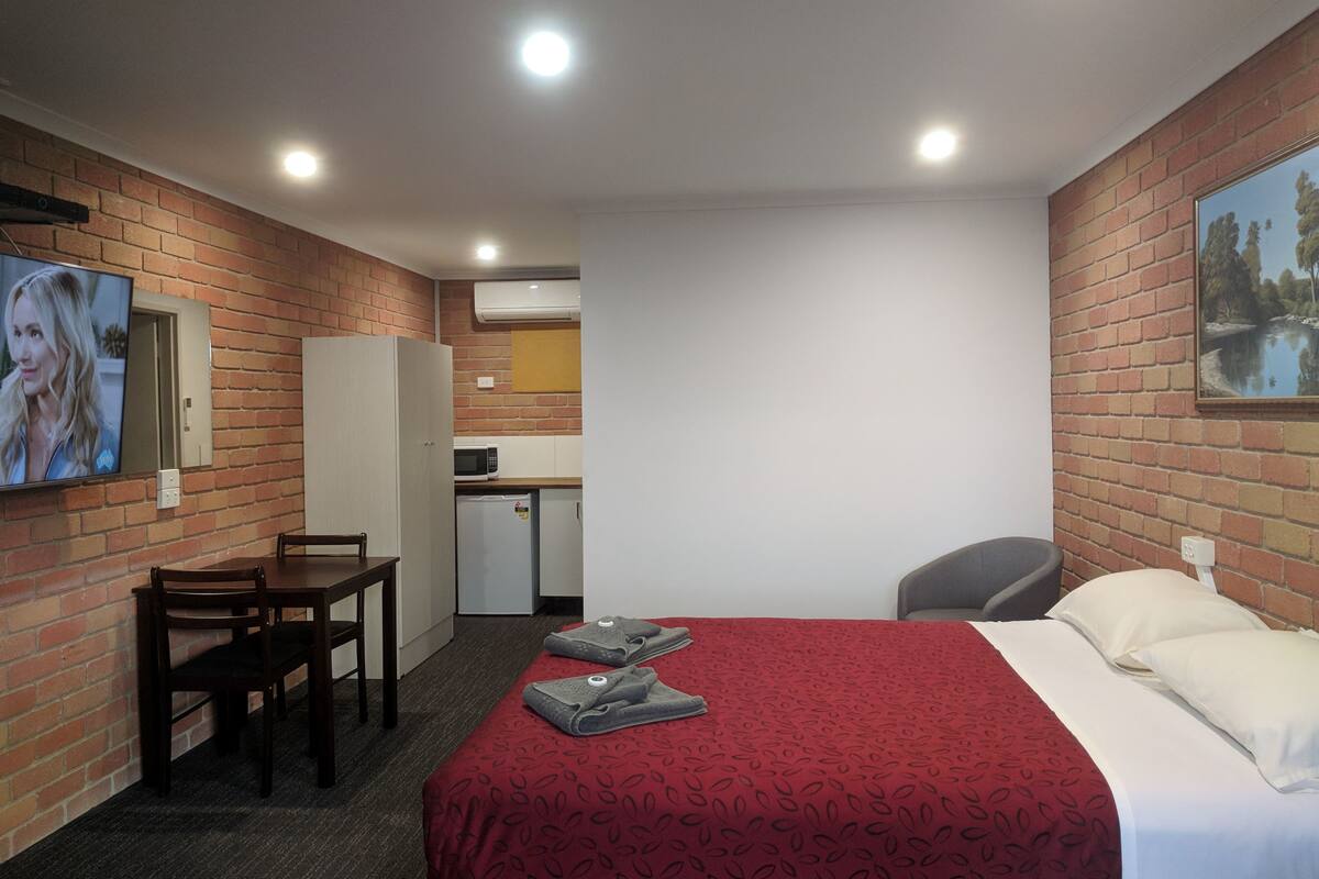 A hotel room with a bed, a desk, a chair, a TV, and a small kitchenette.