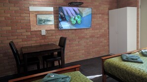 Quarto com parede de tijolos, mesa de jantar com cadeiras, TV fixada na parede e um guarda-roupa.