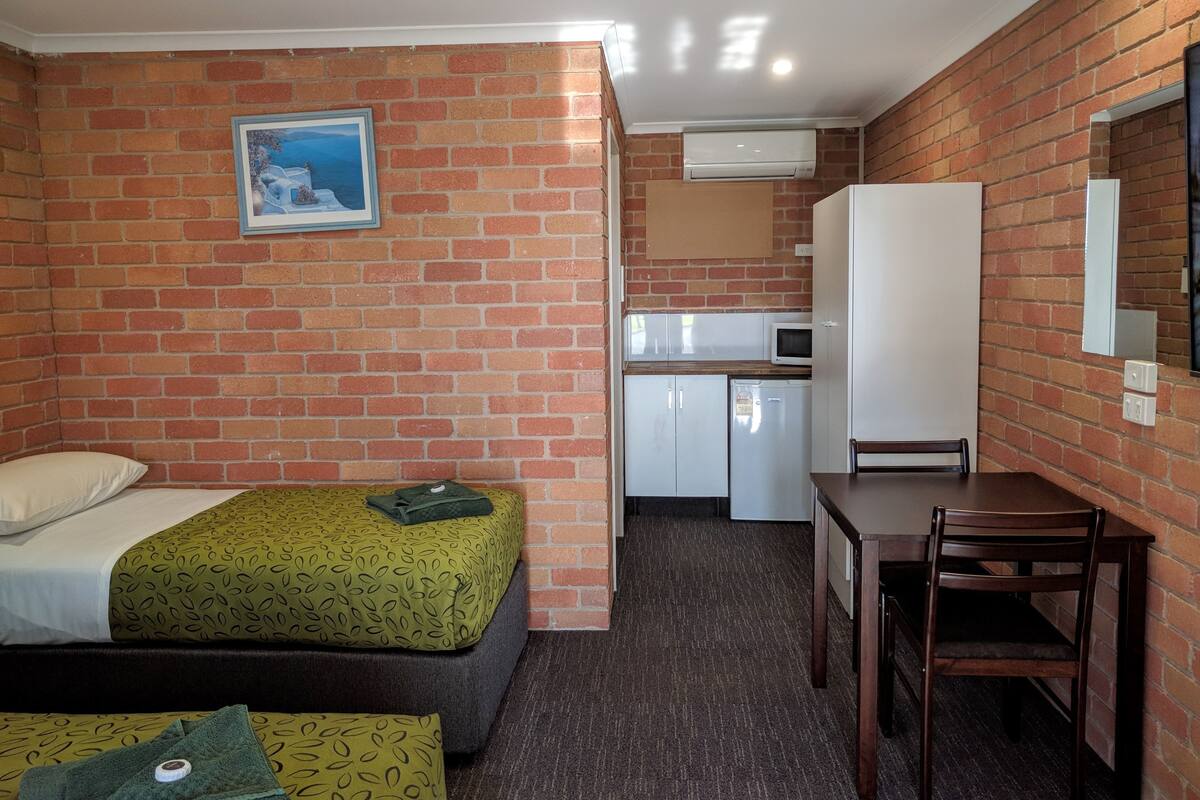 A compact room with a bed, a small kitchenette, a desk, and a chair.