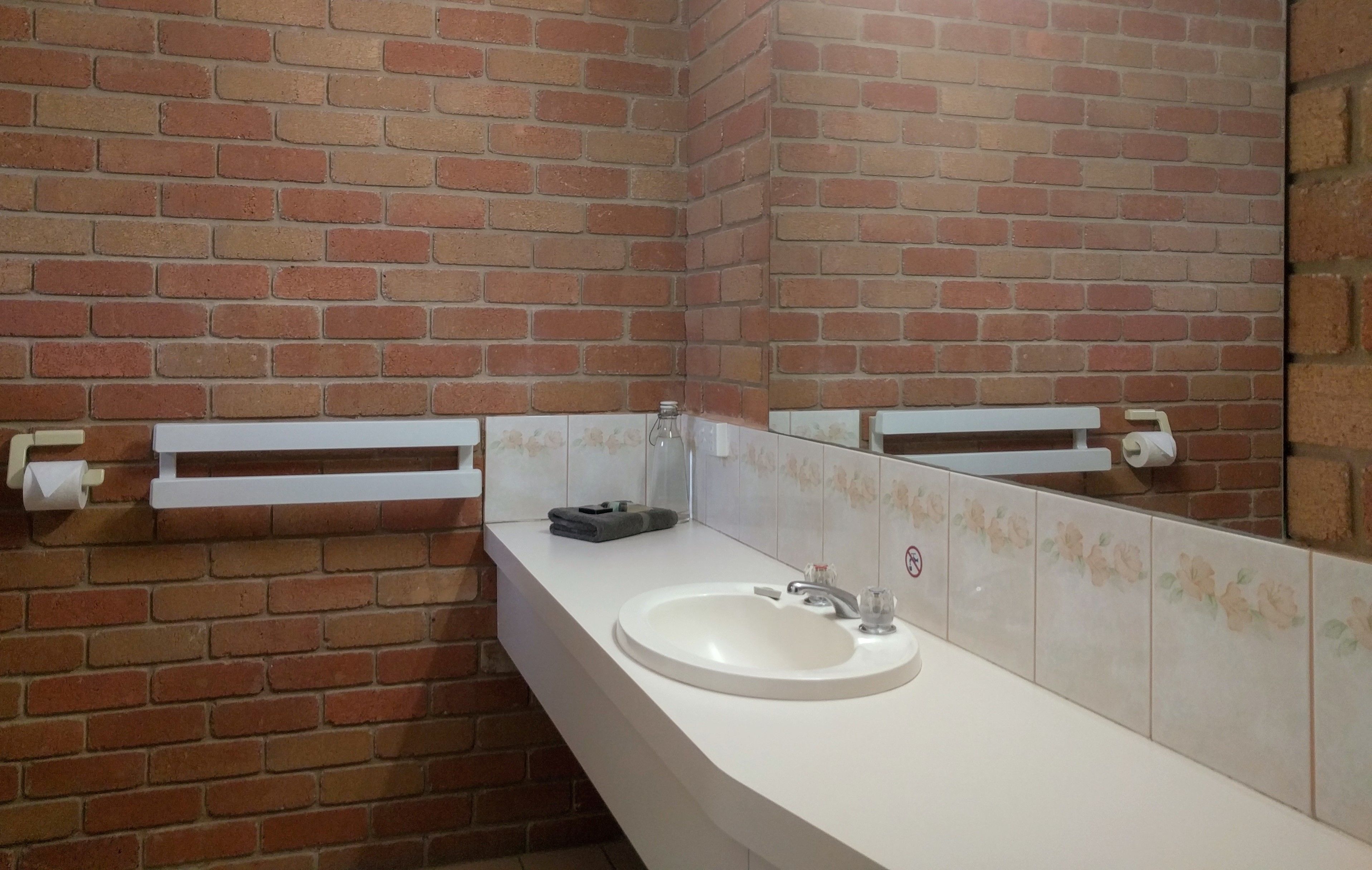 A bathroom with a white sink, a mirror, and a brick wall.