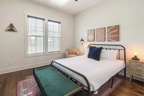A bedroom with a bed, a chair, a bedside table, and a lamp.