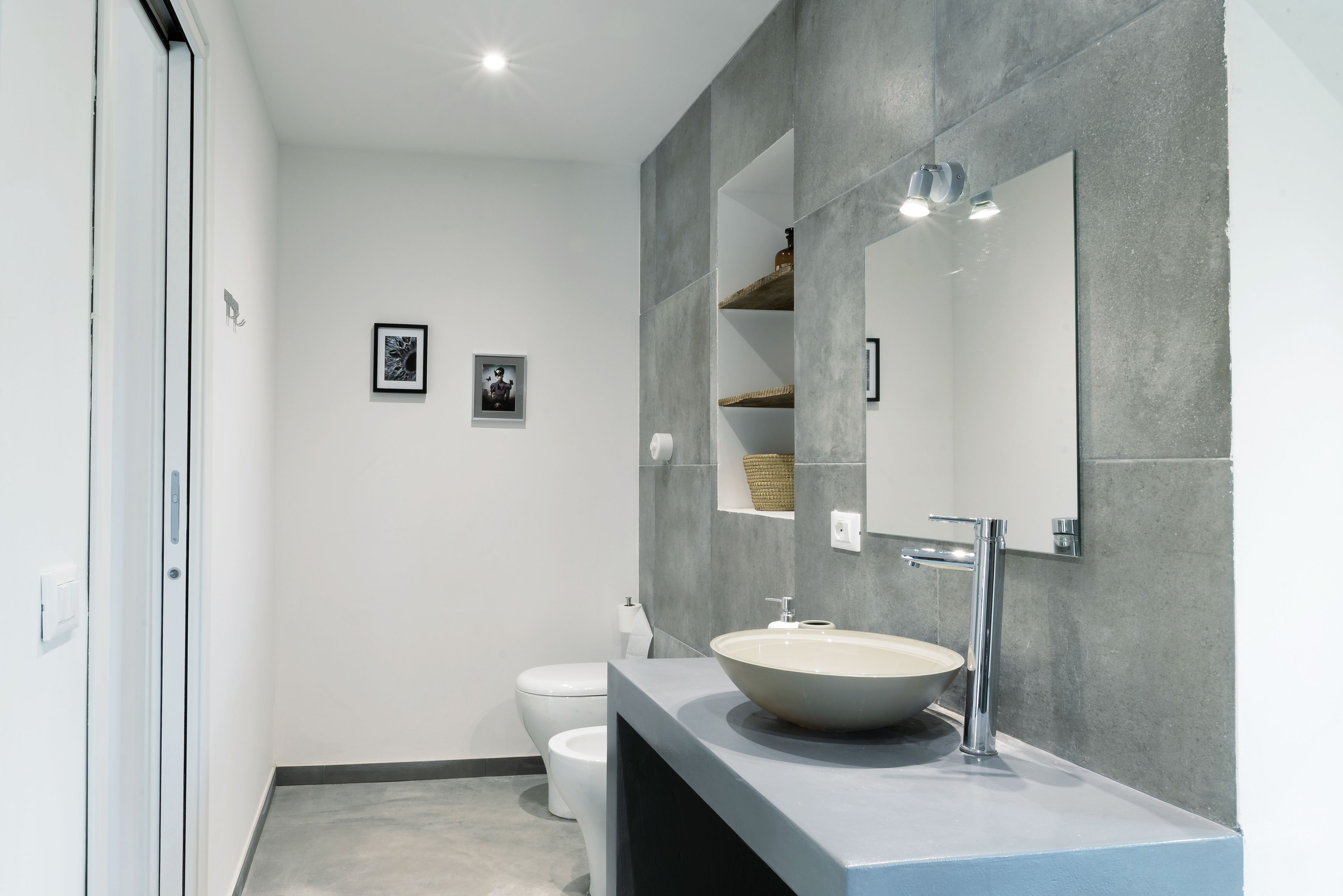 A modern bathroom with a large mirror, a white sink, and a toilet.