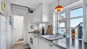 Moderni keittiö, jossa on valkoiset kaapit, ruostumattomasta teräksestä valmistettu allas ja ikkuna, josta on näkymä ulos.