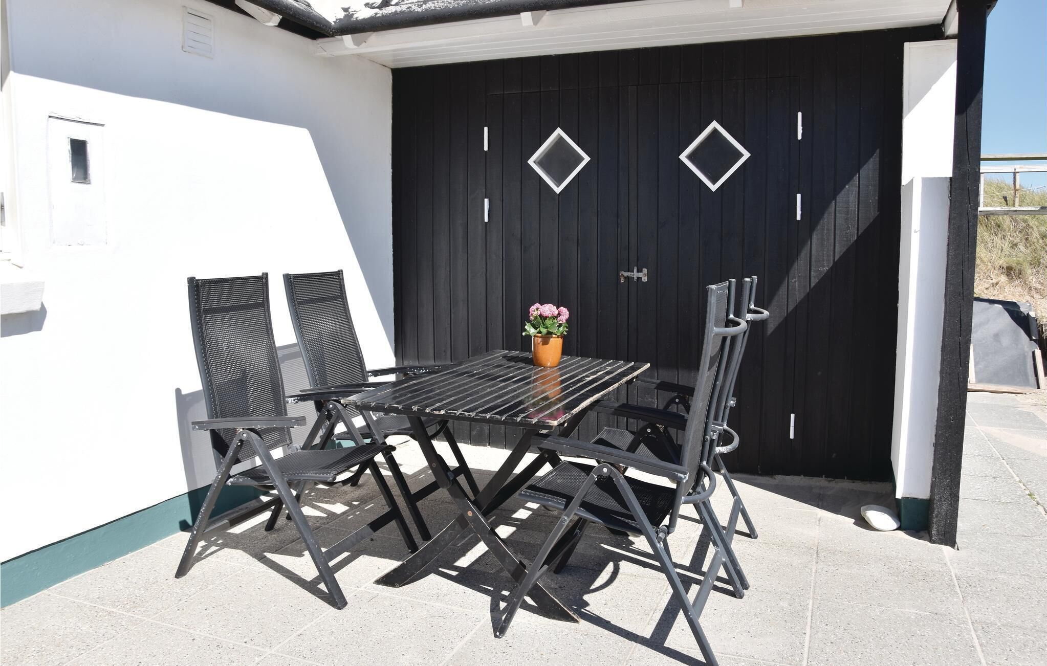 A patio area with a black metal table and chairs, a potted plant, and a black door with diamond-shaped windows.