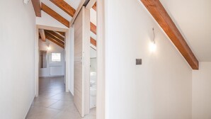 A hallway with a sloped ceiling, wooden beams, and a view into a room with a window and radiator. - 3 bedroom lovely home in Cisano sul Neva (Cisano sul Neva)