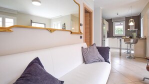 A modern living room with a white sofa, two pillows, a large mirror, and a kitchen in the background. - 3 bedroom lovely home in Cisano sul Neva (Cisano sul Neva)